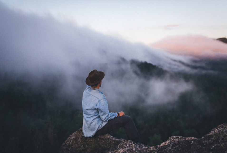Wanderer auf Felsen vor nebligen, bewaldeten Hängen