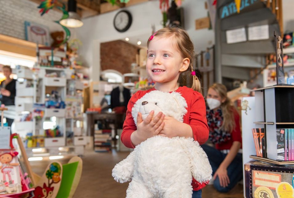 Mädchen mit Teddybär in den Armen in einem Spielzeugladen